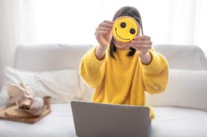 Girl in a yellow sweater sits on the couch in front of a laptop and holds a yellow cookie.